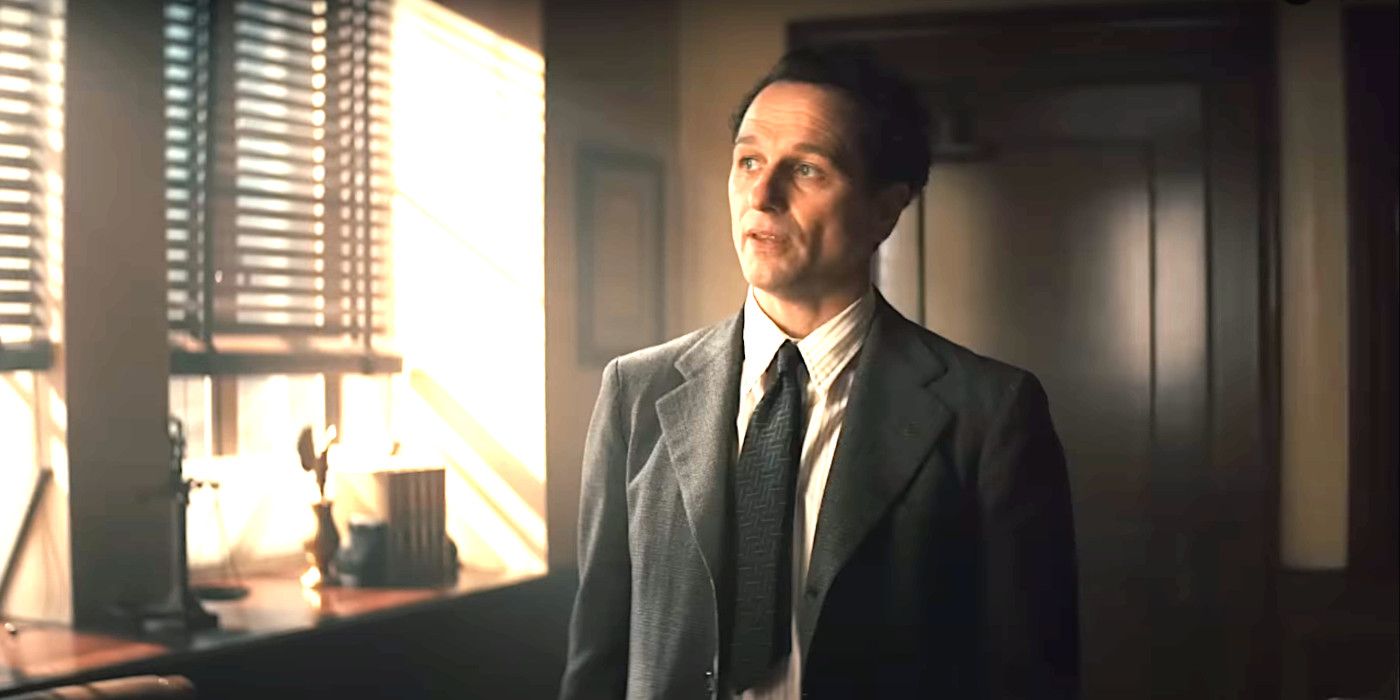 Matthew Rhys In Perry Mason Season 2 in a 1930s suit standing in an office talking while light beams through the Venetian blinds