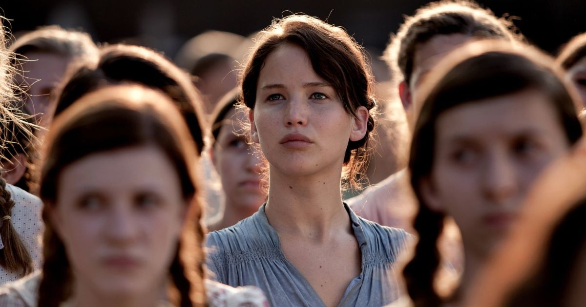 Jennifer Lawrence as Katniss Everdeen in The Hunger Games, standing in a crowd of similarly dressed women.