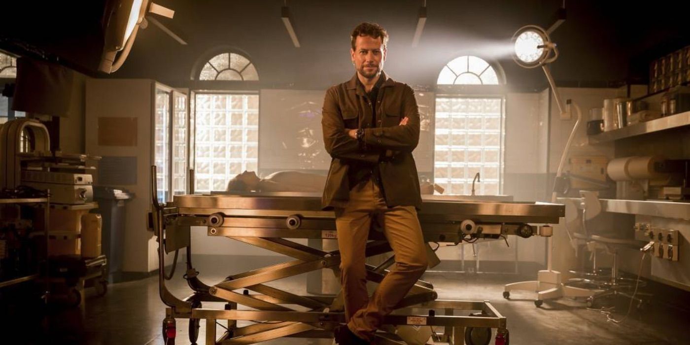 Harrow crosses his arms in front of a medical table in Harrow