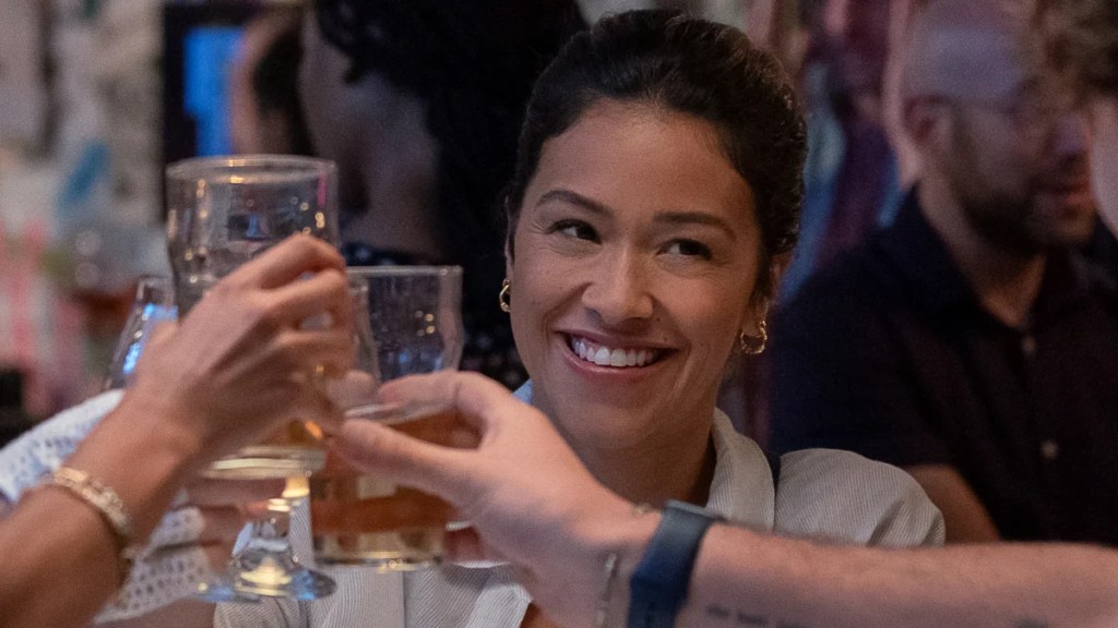 Gina Rodriguez sourit et lève son verre sous les acclamations dans une image de la série Players de Netflix.