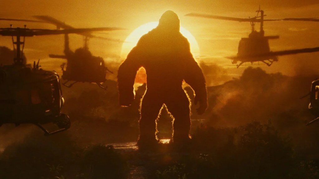 King Kong se tient au coucher du soleil tandis que des hélicoptères survolent