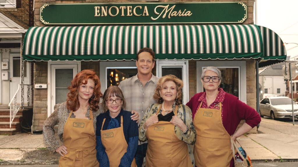 Vince Vaughn se tient en souriant derrière quatre femmes plus âgées portant des tabliers devant Enoteca Maria, un restaurant de Staten Island réel connu pour sa gamme rotative de grands-mères cuisinant une cuisine internationale. Les femmes, chacune avec une personnalité distincte, se tiennent fièrement devant l'avant à rayures vertes et blanches de la boutique sous le panneau à collier or.