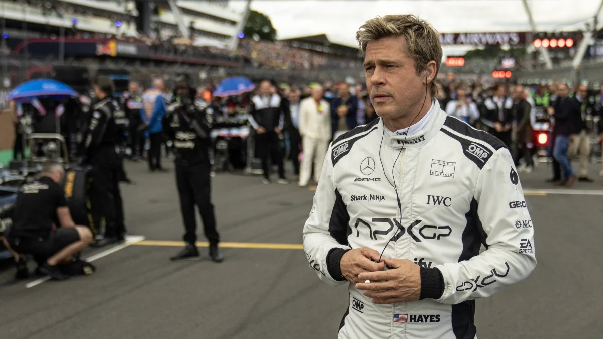 Brad Pitt walks on an F1 track in uniform wearing earbuds in