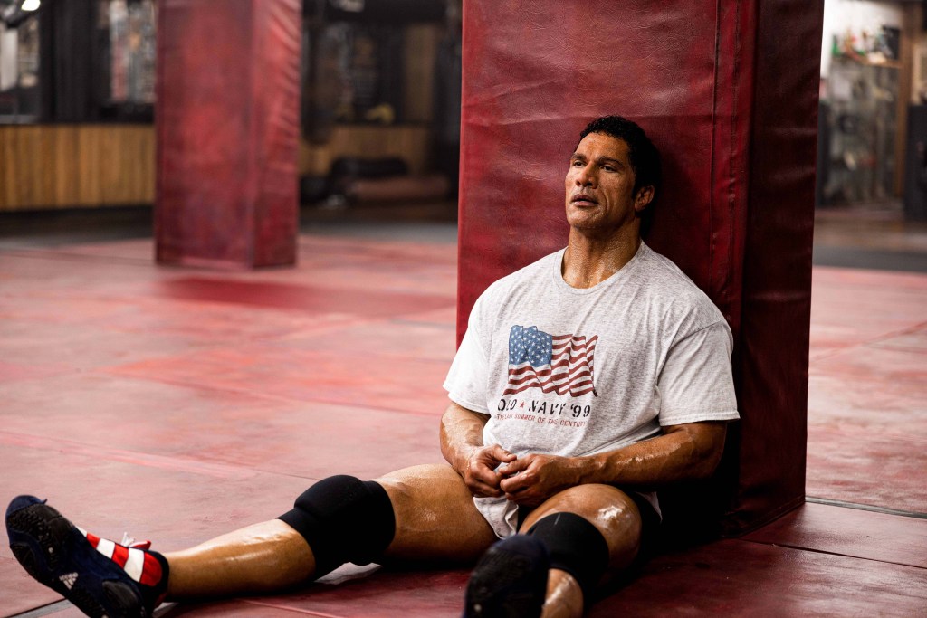 Dwayne Johnson se repose contre un tapis dans une salle de sport dans "The Smashing Machine"